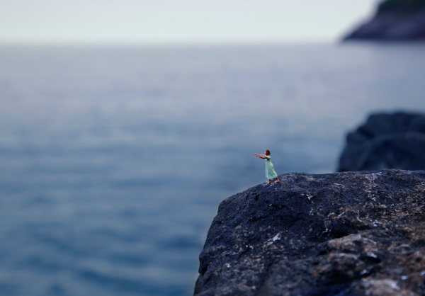An HO scale figurine of a sleepwalking person walking on rocky cliffs above the seaf
