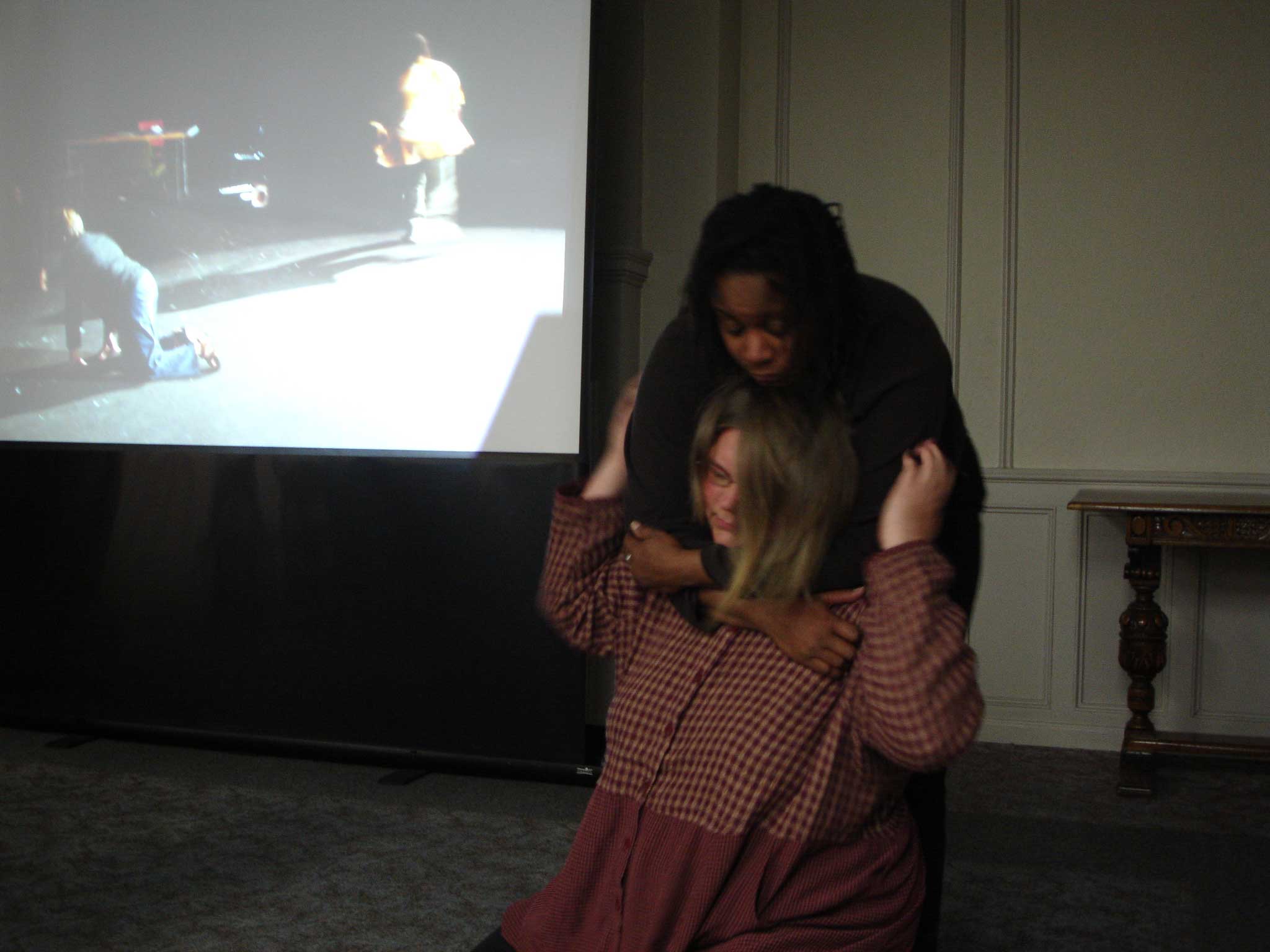 Anita and Petra dancing together, cradling and comforting each other, in front of a projection screen that shows Carrie dancing in the theatre in Montgomery